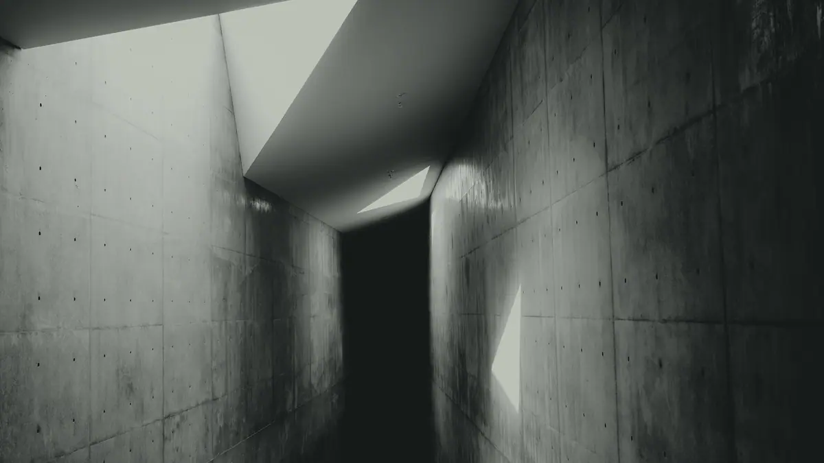 Corredor de concreto atravessado por um recorte de luz vindo do alto.